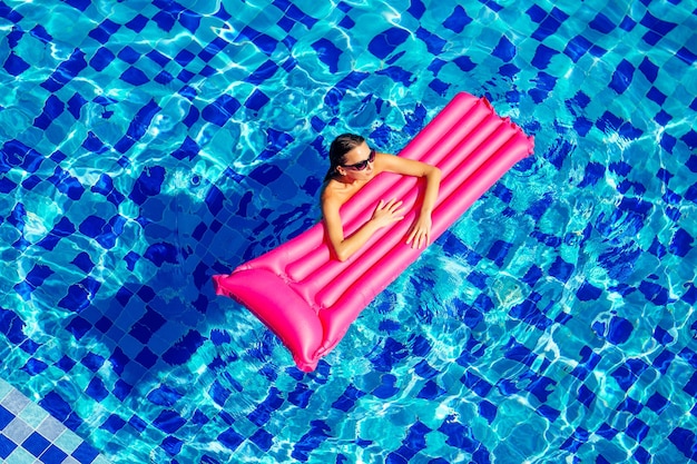 복사 공간 Spf 및 자외선 차단제 수영장 물에 떠 있는 아름다운 브루네트 소녀는 파란색 수영장 원격 작업 및 프리랜서 평면도에서 분홍색 팽창식 매트리스에서 수영하고 휴식을 취합니다.