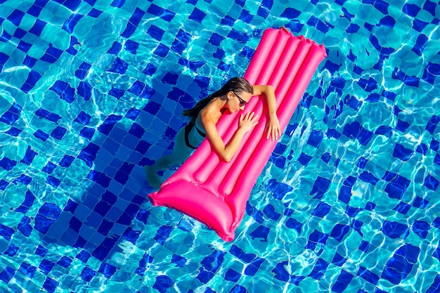 Copy space spf and sunscreen beautiful brunette girl floating in the pool water.woman swimming and relaxing on pink inflatable mattress in blue swimmingpool remote work and freelance top view