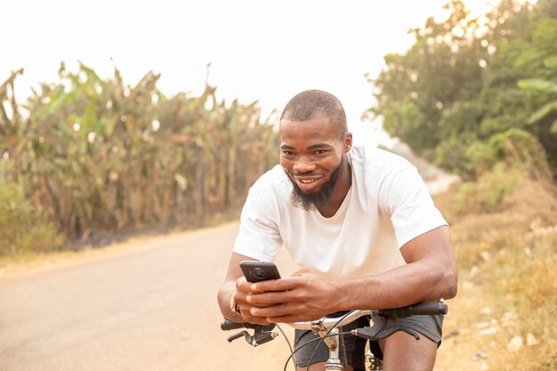 Copy space of young black man smiling using phone while sitting on bicycle