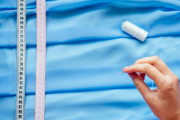 Copyspace close-up blue chiffon, threads and measuring tape seamstress tailor ( dressmaker) designer wedding dress sews beads to lace on a blue background in the studio