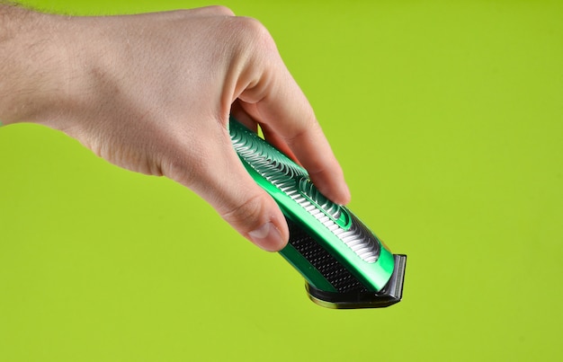 Cordless clipper in a male hand isolated on a green background