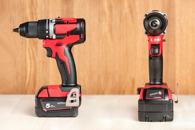 Cordless drill in black and red a screwdriver with a drill lies on a wooden background modern carpen...