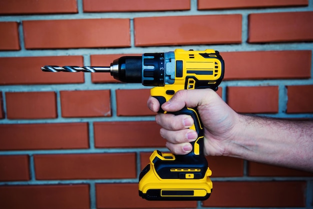 Cordless drill and a drill in the hands of man against the background of a brick wall