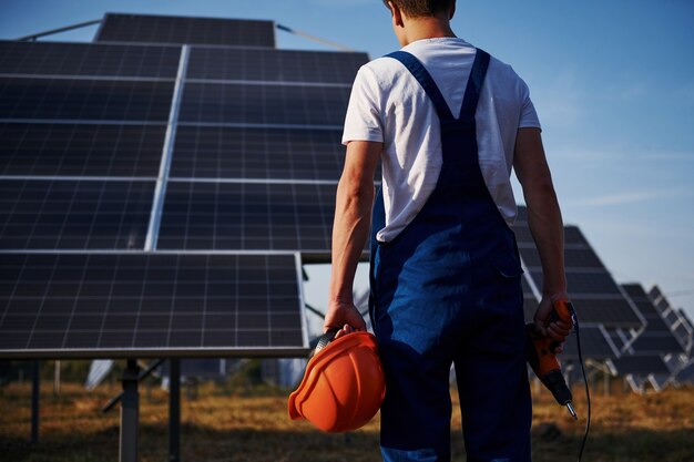 コードレスドライバー。晴れた日に太陽電池で屋外の青い制服を着た男性労働者。