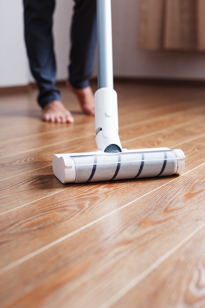 A cordless vacuum cleaner cleans the parquet in the living room with the lower part of the legs.