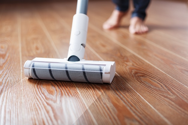 A cordless vacuum cleaner cleans the parquet in the living room with the lower part of the legs.