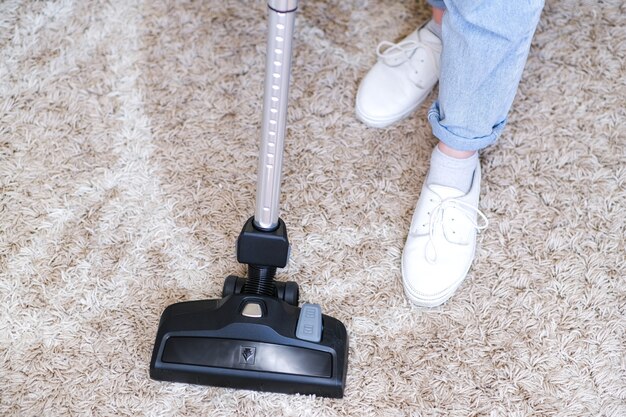 Cordless vacuum cleaner is used to clean the carpet in the room. Housework with a new handheld vacuum cleaner. House cleaning, care and technology concept.