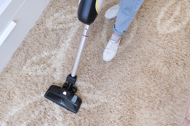 Cordless vacuum cleaner is used to clean the carpet in the room. Housework with a new handheld vacuum cleaner. House cleaning, care and technology concept.