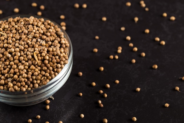 Coriander grains in a glass bowl are scattered on a black . , copyspace.