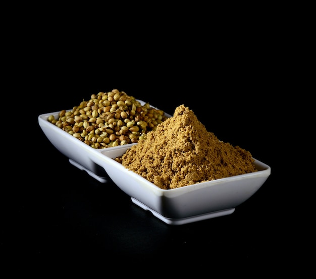 Coriander seeds and Coriander Powder in white plate on black background.