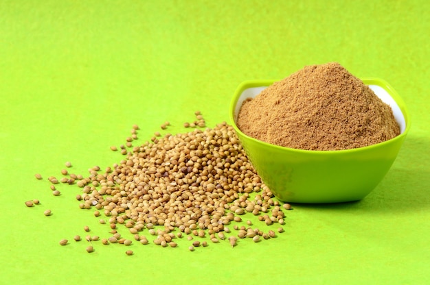 Coriander seeds and Powdered coriander in green container on green surface