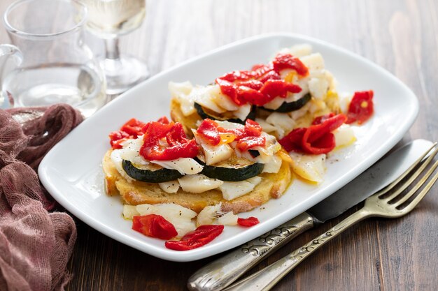 Corn bread with cod fish and courgette on white dish