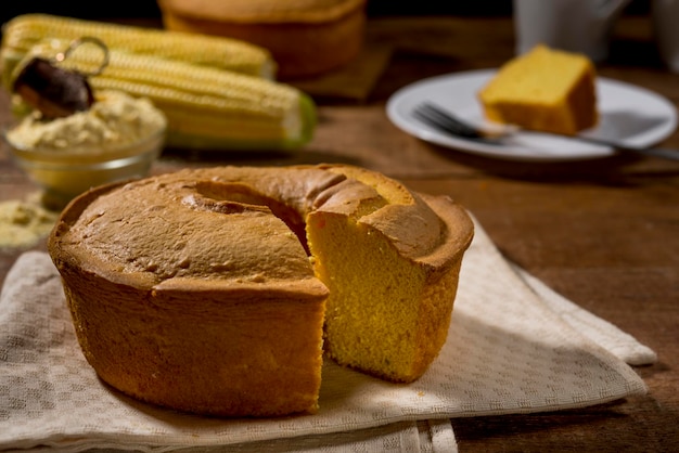 Corn cake witout slice on rustic wood and fabric with corn, slice in plate and cake in background.