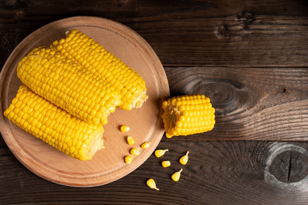 Corn cob with lies on round cutting board plate wooden table . copyspace