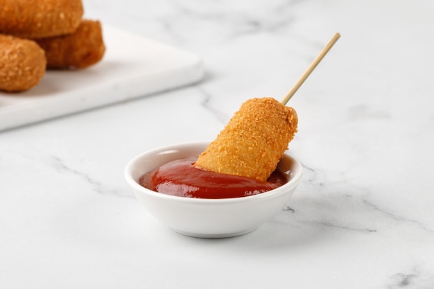 Corn dog met ketchup rode saus op witte marmeren achtergrond Gebakken worst op een stokje Sorn dog corndog