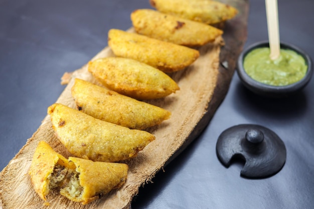 Corn empanada typical Colombian food with spicy sauce on a wooden log