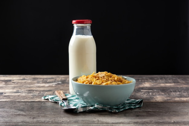 Corn flakes in a blue bowl and milk bottle on wooden table