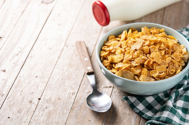 Corn flakes in a blue bowl and milk bottle on wooden table