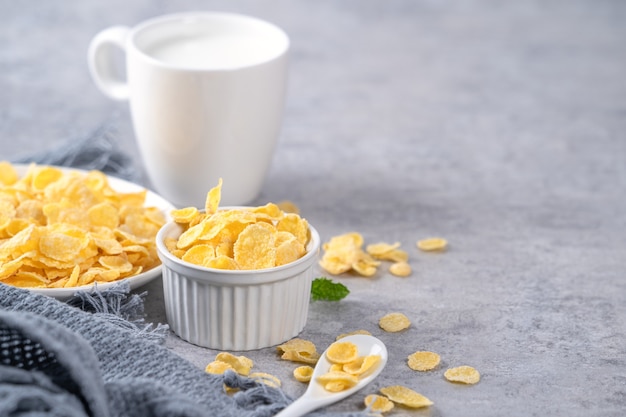 I fiocchi di mais ciotola dolci con latte su sfondo grigio cemento, close up, concetto di design colazione fresca e sana