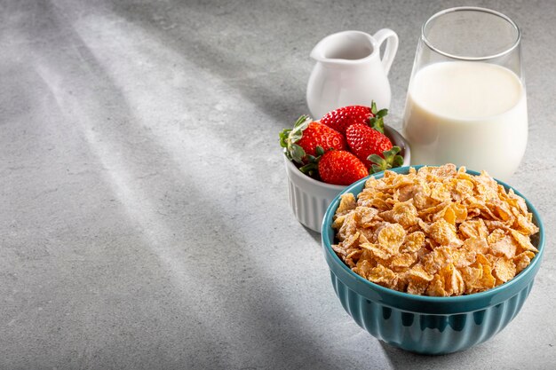 Corn flakes in the bowl with berries and milk on the table