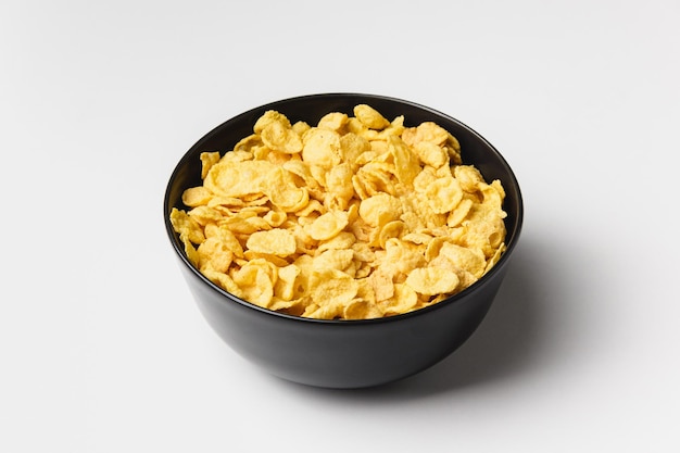 Corn flakes in dark bowl on white background