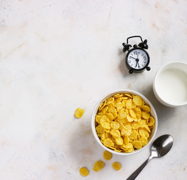 Photo corn flakes, milk, alarm clock on a light background