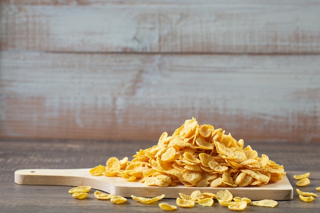 Corn flakes(whole grain) on wooden chopping board on table.