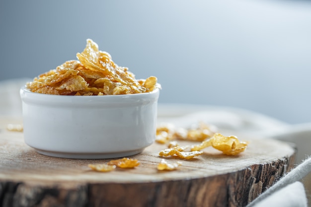 Corn flakes with honey in white bowl on wooden surface. Copy space