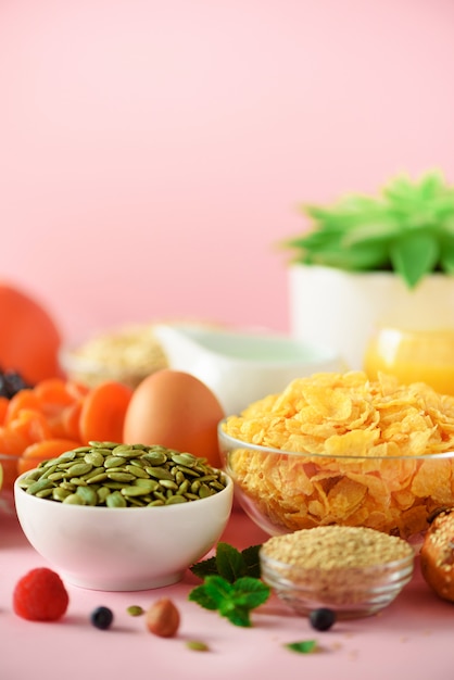 Corn flakes with milk, fresh berries, yogurt, boiled egg, nuts, fruits, orange, banana, peach for breakfast on yellow background. Copy space. Healthy food concept.