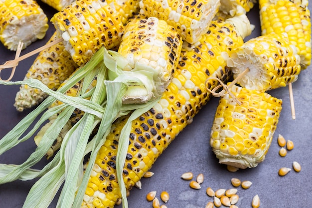 Corn grains and grilled cobs with leaves. Metallic rusty background.