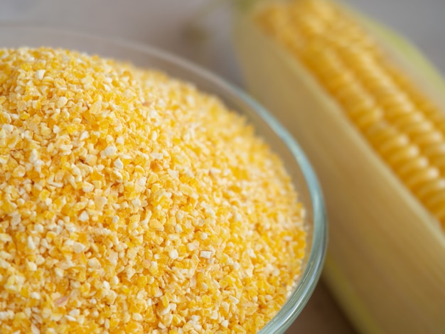 Corn grits in a glass bowl close-up on the background with an ear of corn