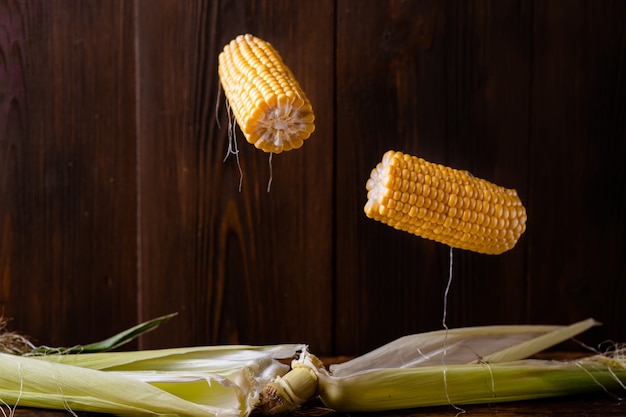 Photo corn levitation. fresh raw corn cobs on a dark wooden background fly in the air. vegetarianism, wholesome food concept.