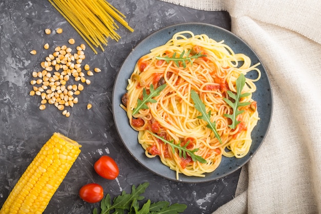 Corn noodles with tomato sauce and arugula on a black concrete surface and linen textile