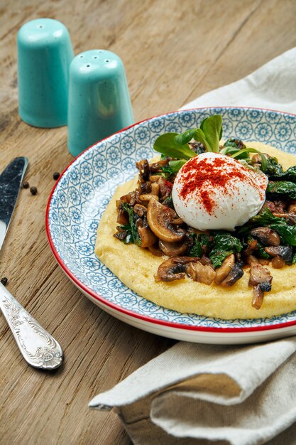 Corn porridge or polenta with fried mushrooms and poached egg in a blue ceramic plate on a wooden surface. Healthy and Diet Breakfast