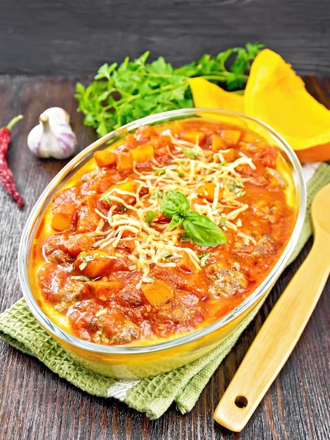 Corn porridge with meatballs, sauce of tomato, garlic and pumpkin, sprinkled with cheese, basil in a pan on napkin on dark wooden board background