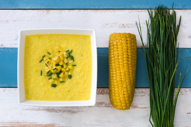 Photo corn soup in bowl on blue and white wooden surface