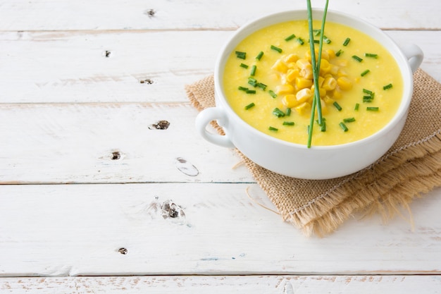 Corn soup in bowl on white wooden surface Copy space