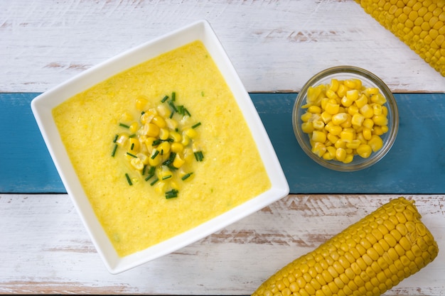Photo corn soup in white bowl on white and blue wooden table top view