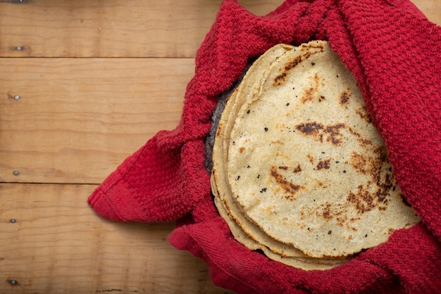 Corn tortillas wrapped in a red cloth on wooden table