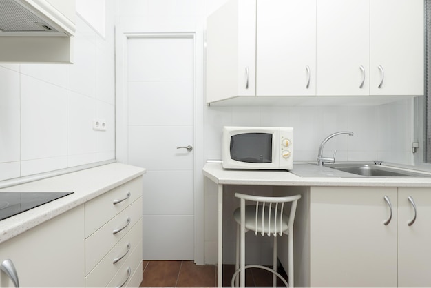 Corner of a humble conventional kitchen with white cabinets and countertops of the same color