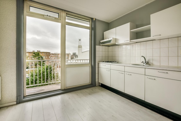 Corner kitchen of a light shade in a minimalist style and access to the balcony in a studio apartment