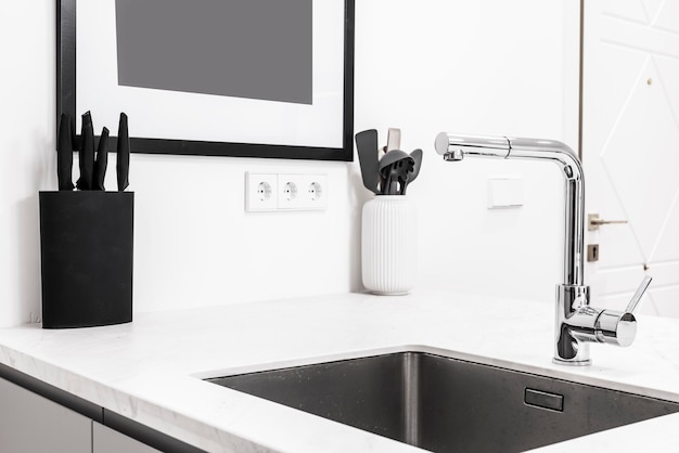 Corner of a kitchen with a white marble countertop a builtin stainless steel sink and a knife rack with black handles