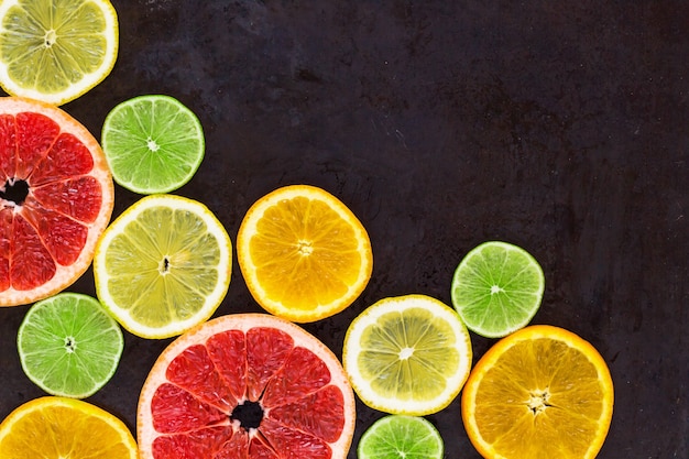 Corner with slice of oranges, lemons, limes, grapefruit on black background. Flat lay, top view