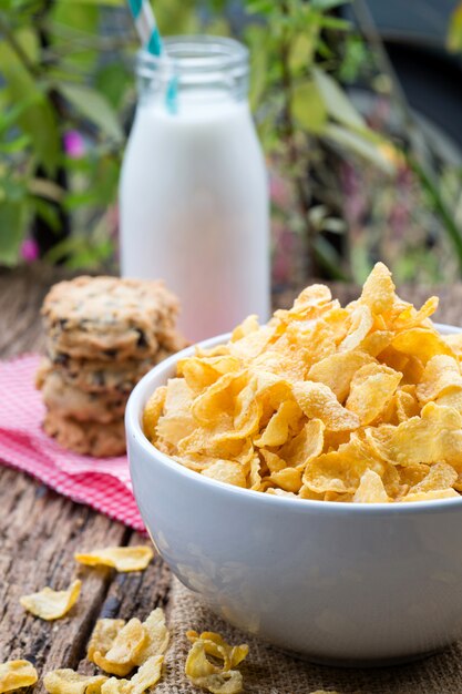 Cornflake cereals on white bowl with milk glass on table.