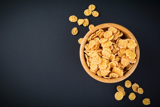 Cornflakes for breakfast in a bamboo plate on dark surface. Selective focus.