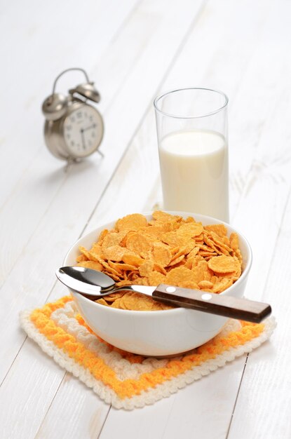 Cornflakes en melk op houten planktafel met wekker