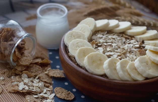 Cornflakes in houten kom en havermout met bananen en melk in een glazen fles