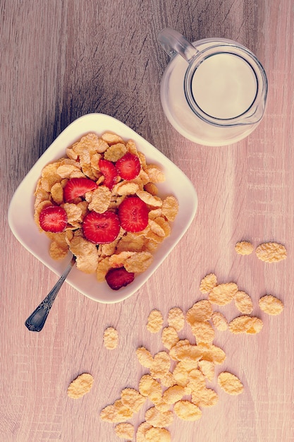 Cornflakes met aardbeien en een kruik melk op houten achtergrond