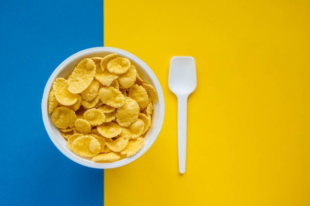 Cornflakes in white bowl with spoon on blue and yellow background