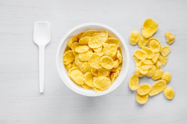 Cornflakes in white bowl with spoon on white wooden background. Top view. Copy, empty space for text